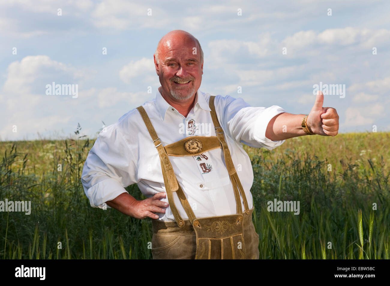 Vieux heureux homme portant costume traditionnel allemand debout dans le champ de céréales avec pouce vers le haut, l'Allemagne, Rhénanie-Palatinat Banque D'Images