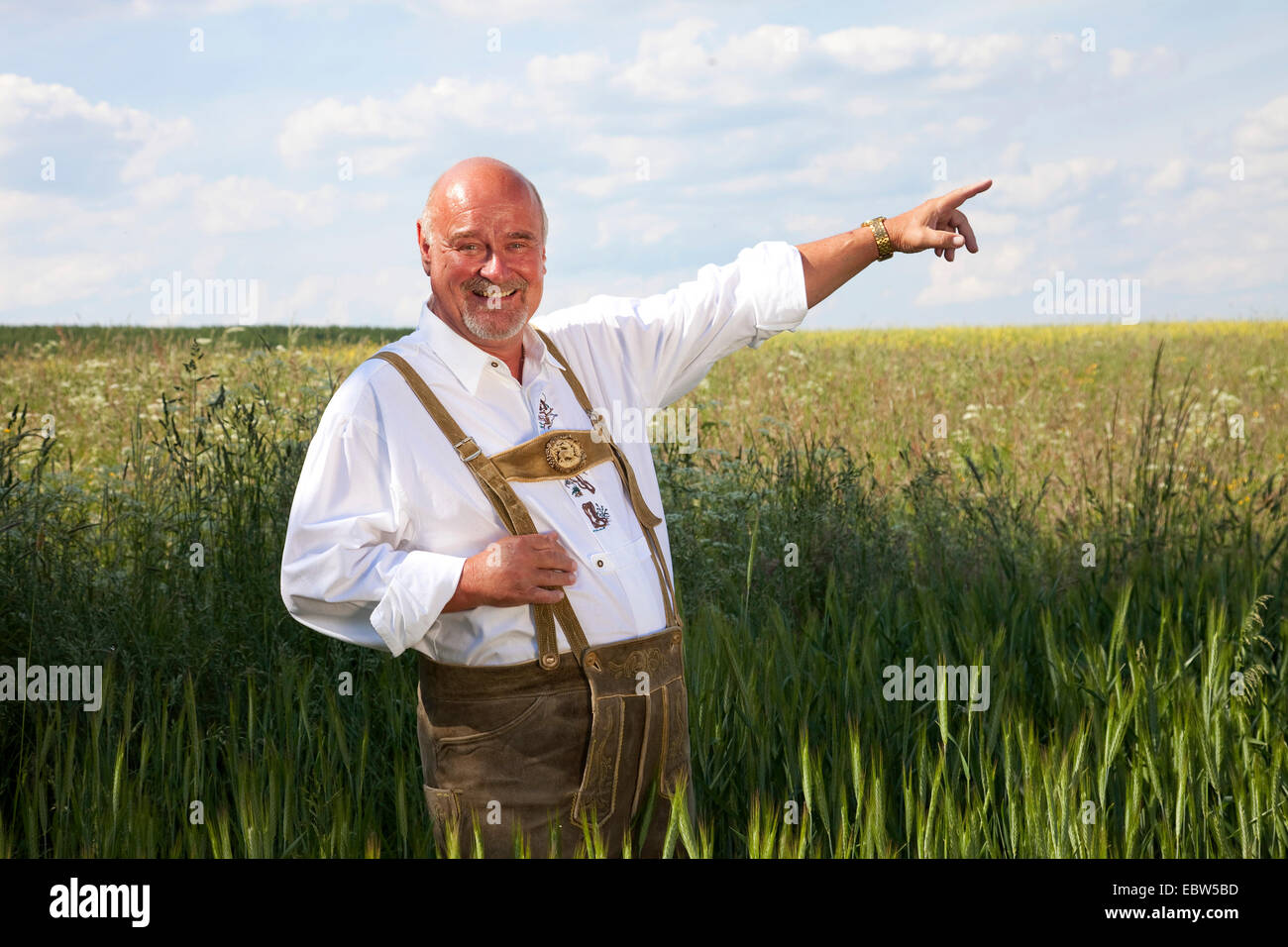 Vieil homme heureux en costume traditionnel allemand standing in grain field et pointant vers le ciel, l'Allemagne, Rhénanie-Palatinat Banque D'Images
