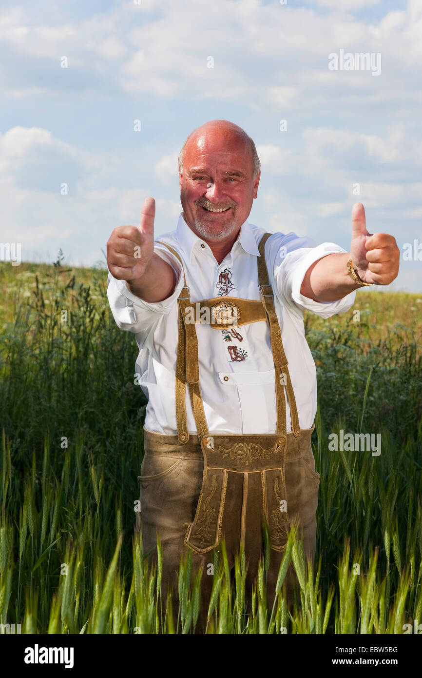 Vieux heureux homme portant costume traditionnel allemand avec Thumbs up standing in grain field, Allemagne, Rhénanie-Palatinat Banque D'Images