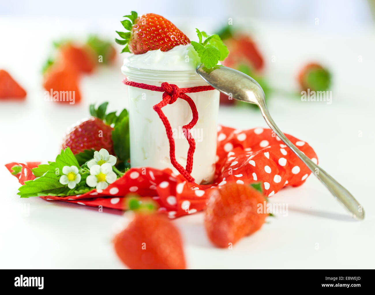 La ferme rouge frais mûrs fraises avec un bocal en verre de yaourt sain servi sur un pays rouge à pois serviette pour un délicieux petit-déjeuner ou apéritif Banque D'Images