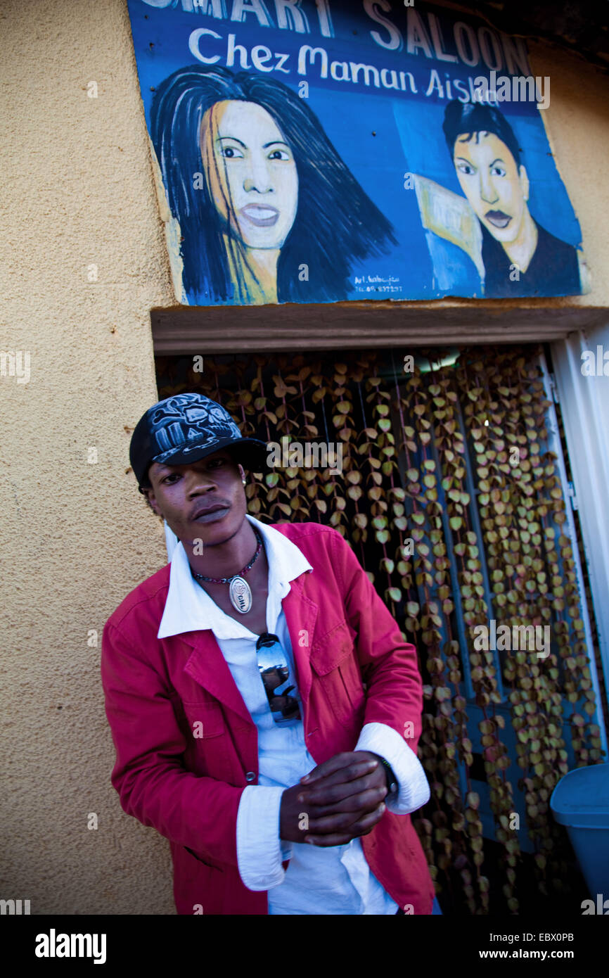 Jeune homme en face d'une boutique de coiffeur qu'il vient de visiter, nommé 'Chez Maman Aisha' , le Rwanda, Kigali, Nyamirambo Banque D'Images