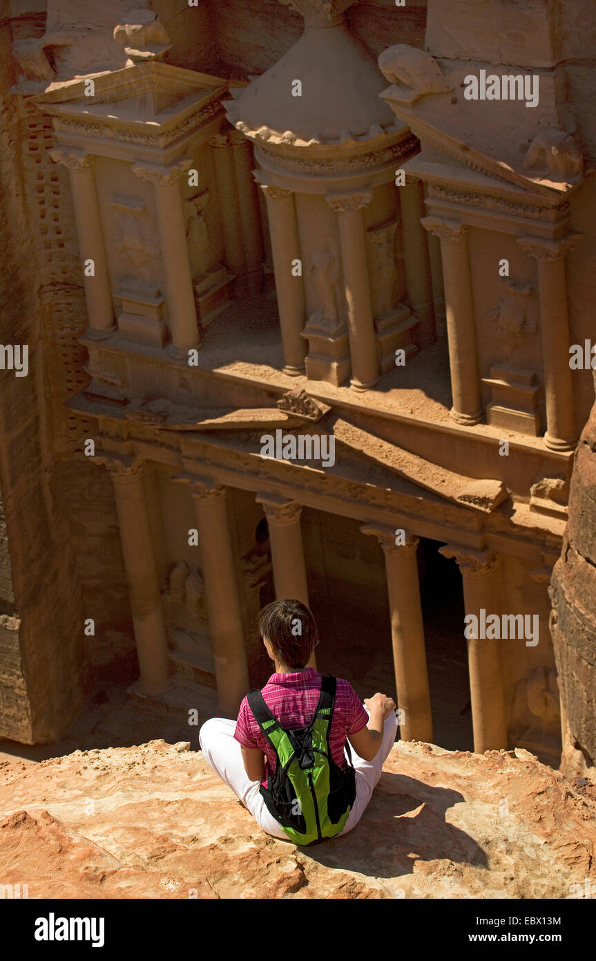 Les jeunes backpacker assis sur un éperon rocheux à la recherche dans le portique du tombeau de roche appelée 'trésor' (Al khazneh) de la ville historique de roche de Petra, Jordanie, Petra Banque D'Images