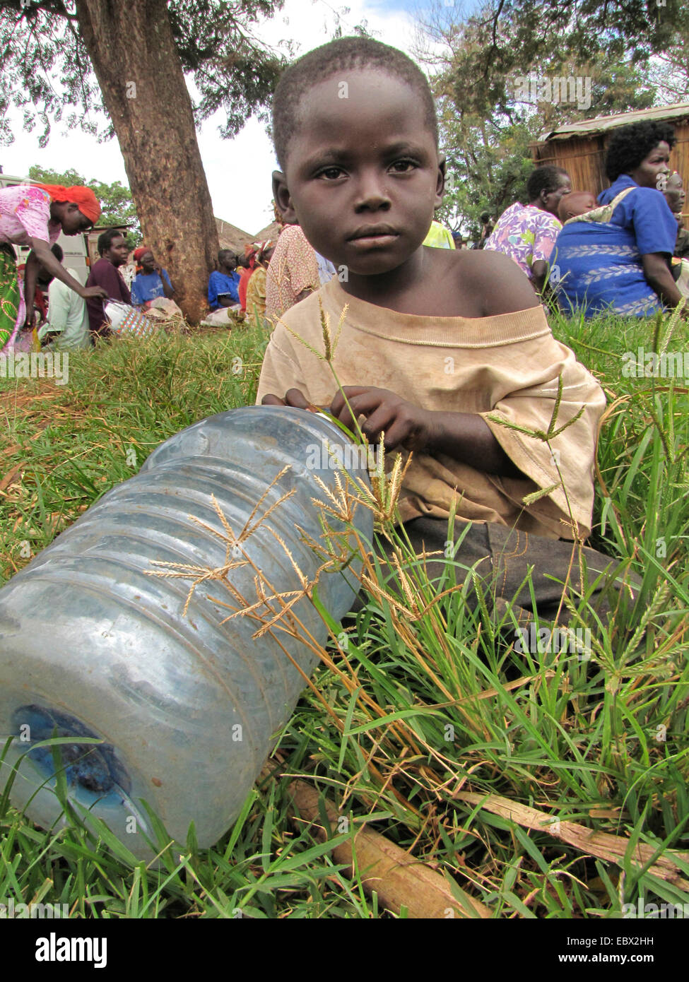 Camp de réfugiés pour les personnes déplacées dans le nord de l'Ouganda autour de Gulu, simple maison de terre en arrière-plan, garçon avec bouteille de plastique est en attente pour l'eau, de l'Ouganda, Gulu Banque D'Images