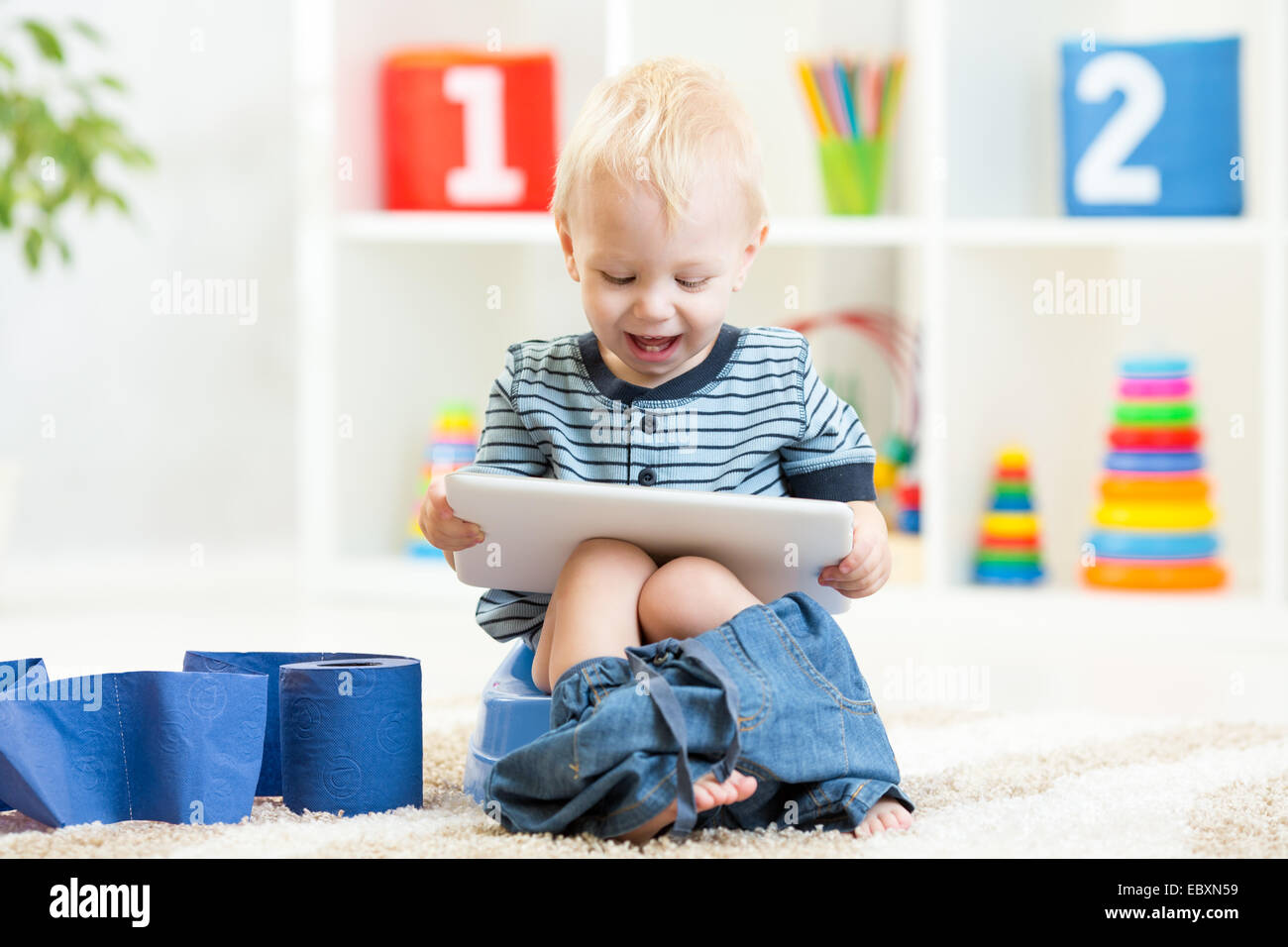 Smiling enfant assis sur le pot de chambre avec du papier toilette Banque D'Images