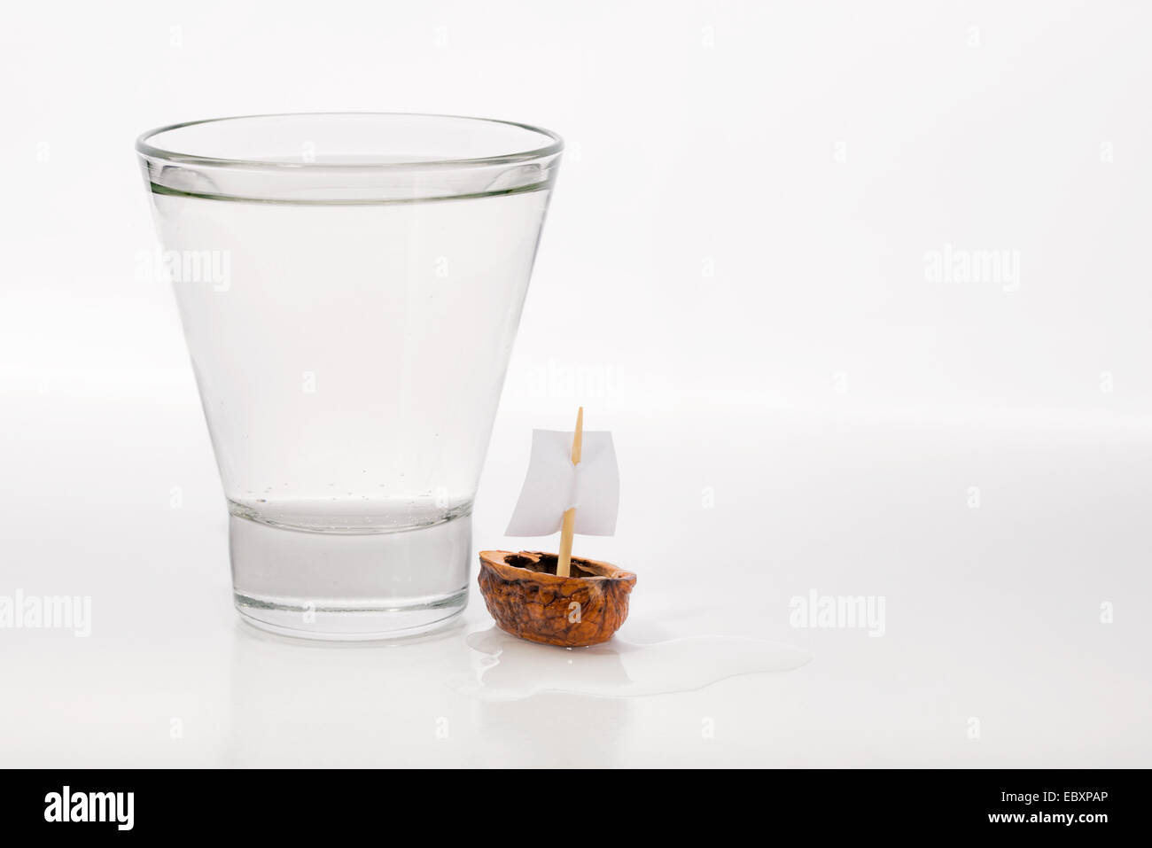Libre d'une coquille de noix avec une voile de bateau, près d'un verre transparent rempli d'eau ou d'alcool. Banque D'Images
