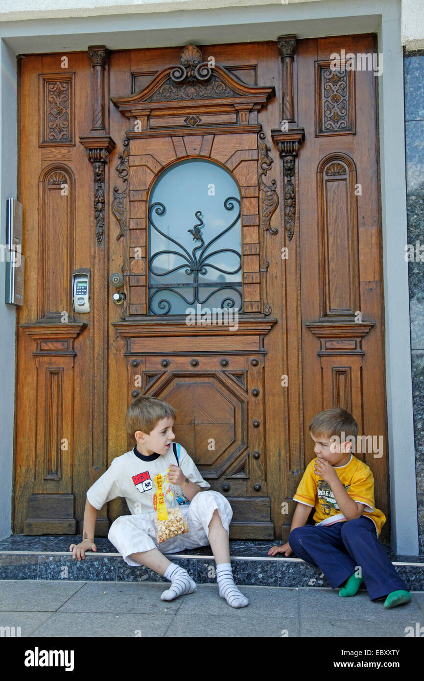 Deux garçons assis en face de la porte d'entrée et eating popcorn Banque D'Images