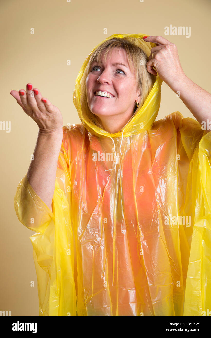 Femme portant un poncho jaune par temps humide tenant sa main pour vérifier s'il pleut Banque D'Images