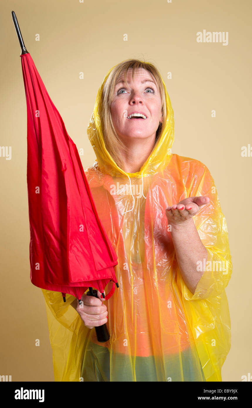 Rain check femme portant un poncho jaune et tenant un parapluie rouge Banque D'Images