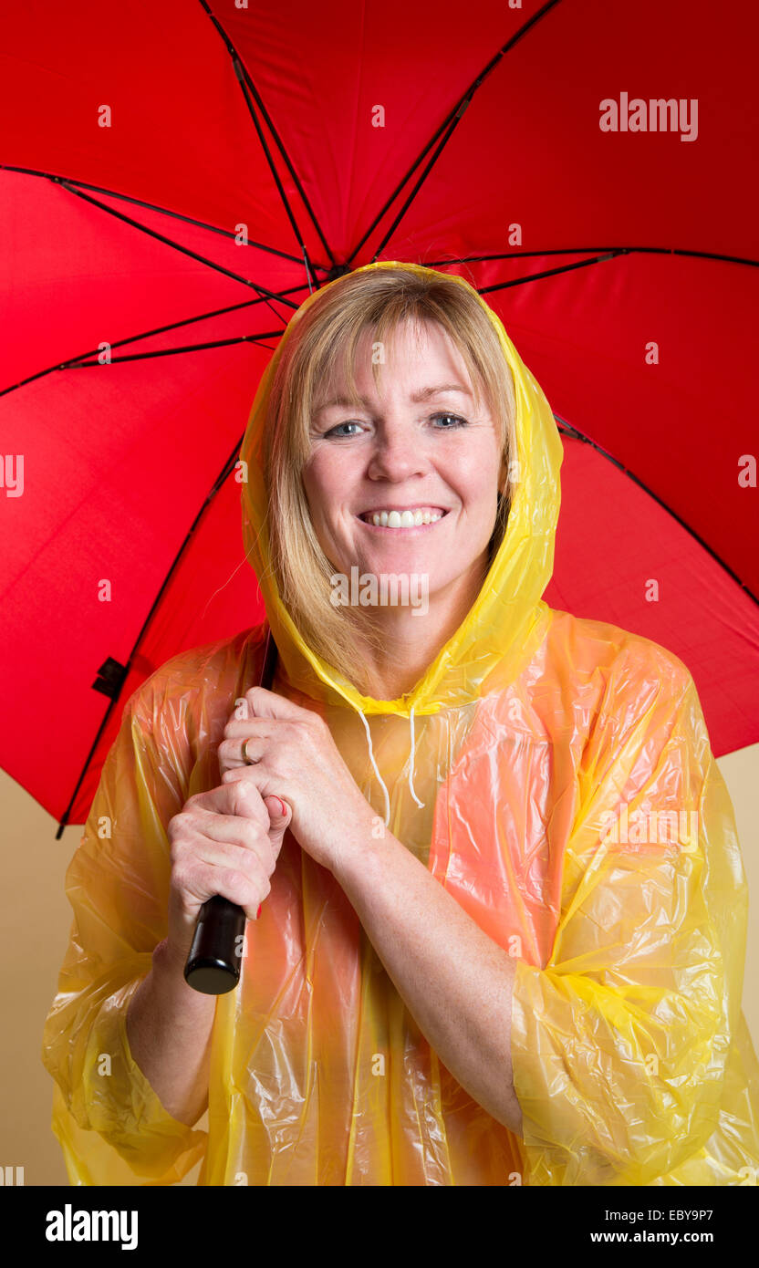 Rain check femme portant un poncho jaune et tenant un parapluie rouge Banque D'Images