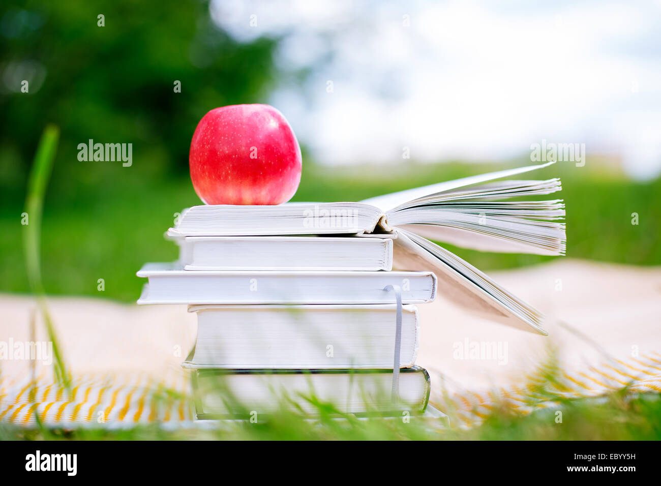 Pile de livres avec un livre ouvert et pomme rouge sur fond nature Banque D'Images