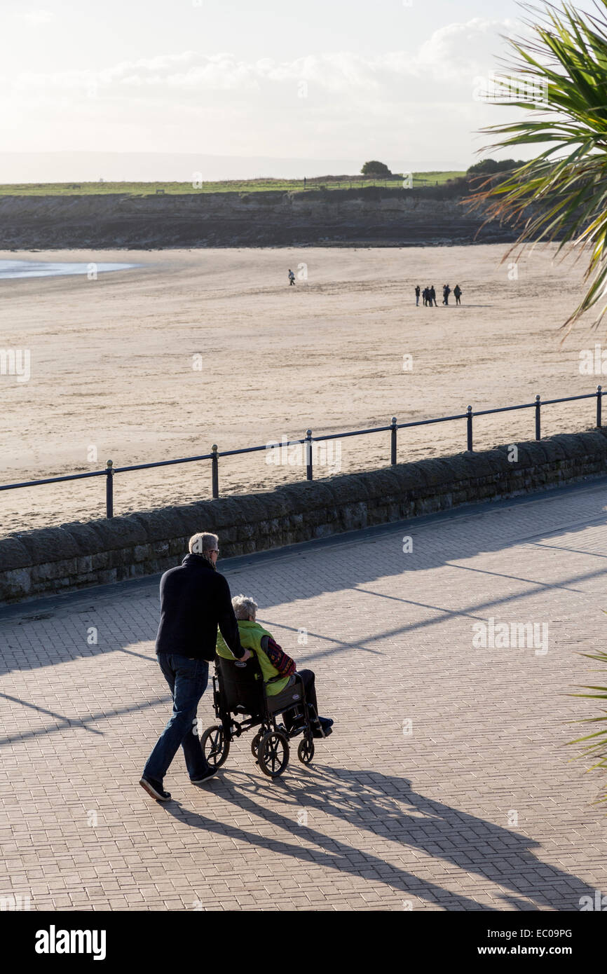 Man pushing wheelchair le long de la promenade, Barry Island, Wales, UK Banque D'Images
