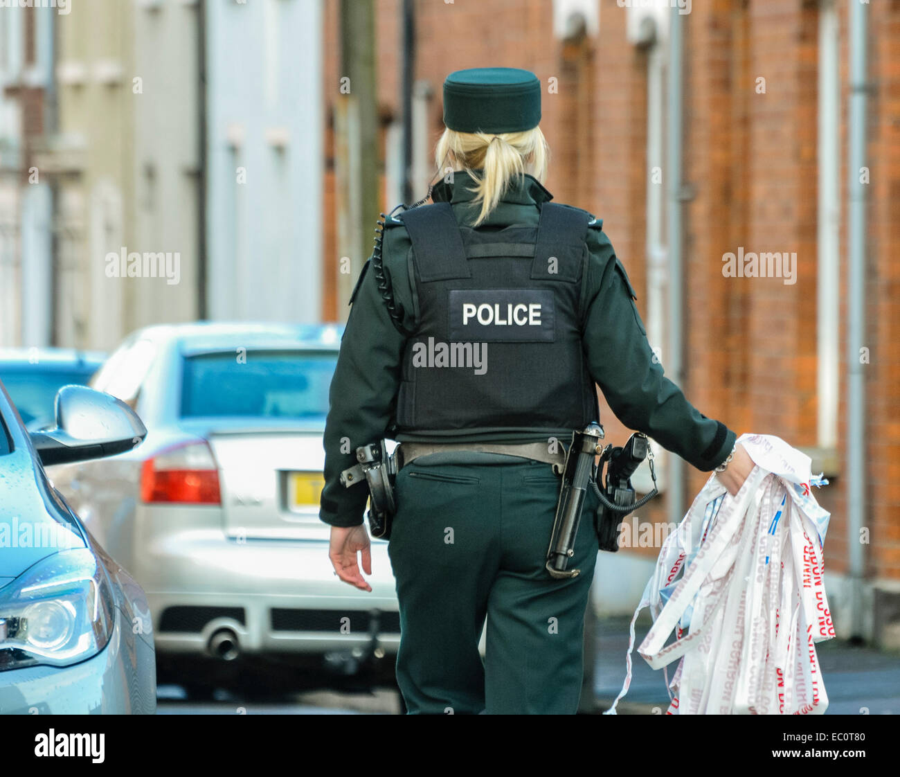 Belfast, Irlande du Nord. 7 décembre 2014 - Un agent de police enlève la bande de cordon à l'extérieur de la maison où un incident domestique a entraîné un homme de 21 ans à être mortellement poignardé tard la nuit dernière. Deux hommes (21 et 25) et une femme (25) ont été arrêtés. Banque D'Images