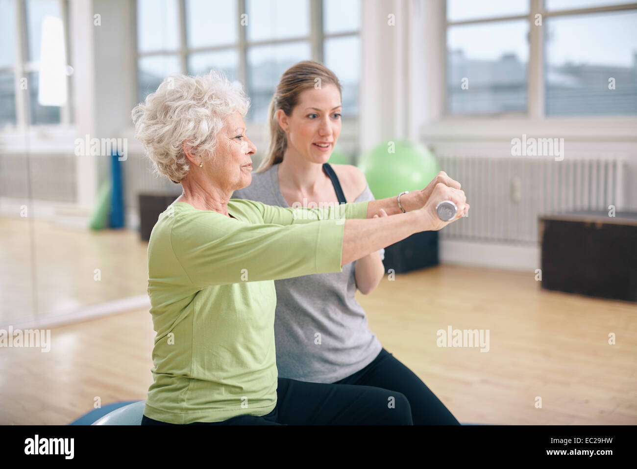 Senior woman étant assisté par l'instructeur pour le levage à gym haltères. Formation Senior woman dans la salle de sport avec un entraîneur personnel Banque D'Images