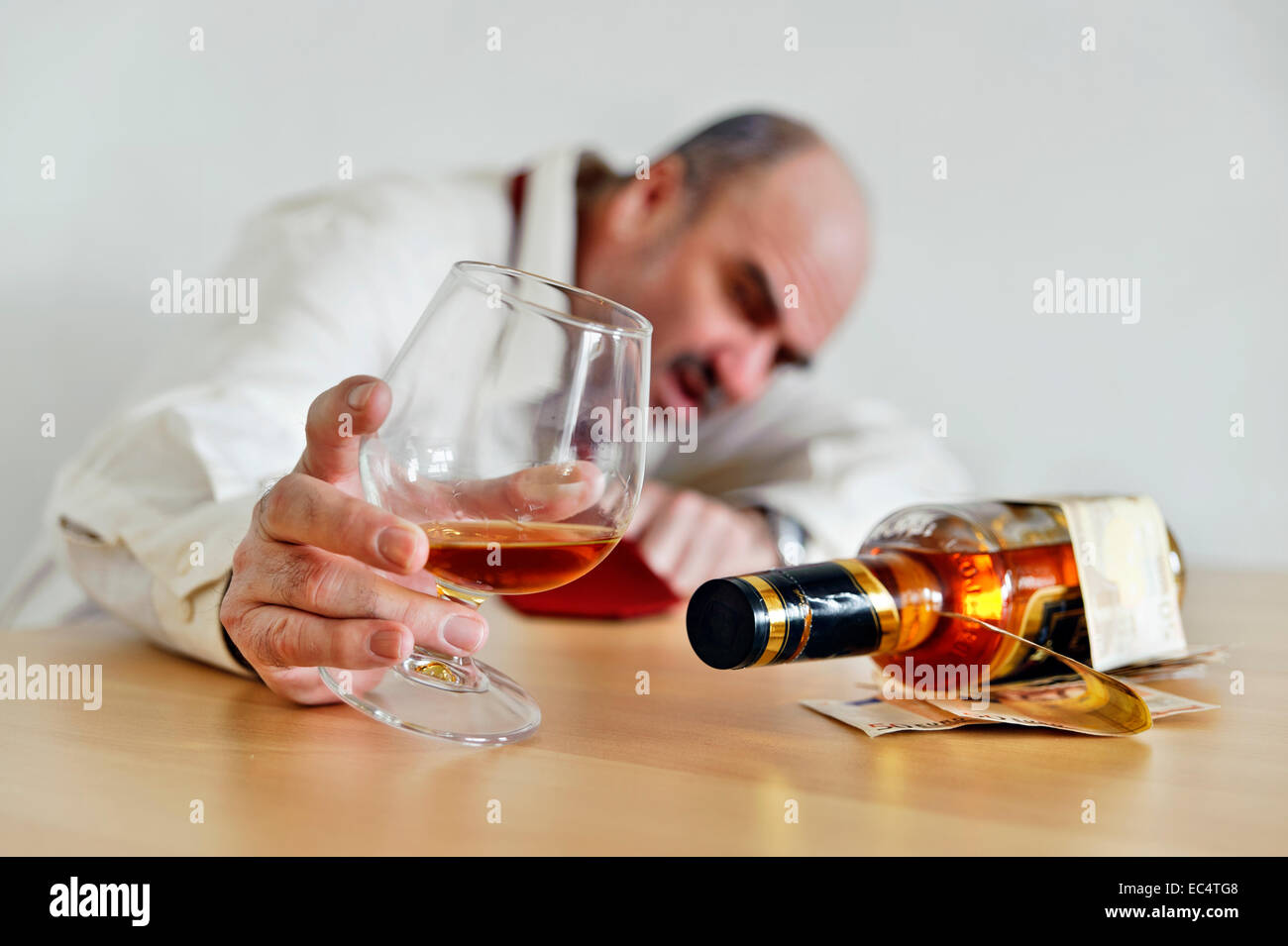 Ivrogne assis avec un cognac et une bouteille de brandy à la table Banque D'Images