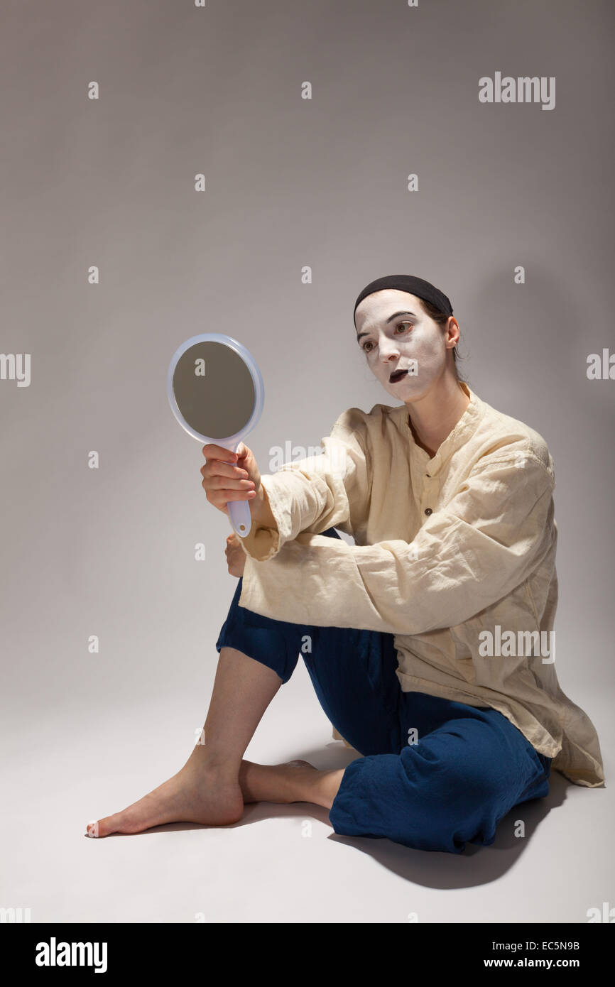 Le clown est assis sur le sol avec un miroir dans sa main Banque D'Images