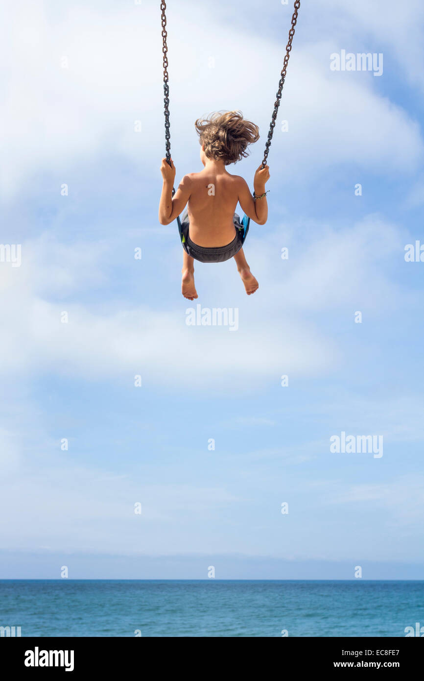 LOS ANGELES, CA - 11 juillet : Boy swinging haut sur une balançoire avec vue sur l'océan à Los Angeles, Californie le 11 juillet 2014. Banque D'Images
