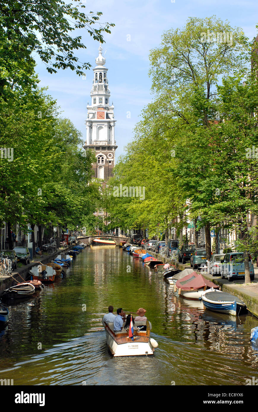 Petite embarcation à moteur au volant dans un canal d'eau dans le centre-ville d'Amsterdam, Pays-Bas avec l'Oude Kerk en arrière-plan. Banque D'Images