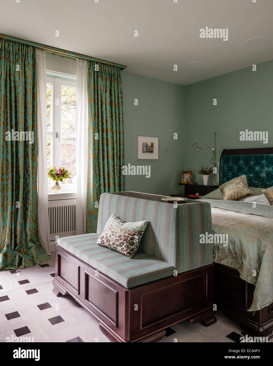 L'aigue-marine sur tête de lit en velours boutonnée, lit dans la chambre avec des rideaux vert et or Banque D'Images