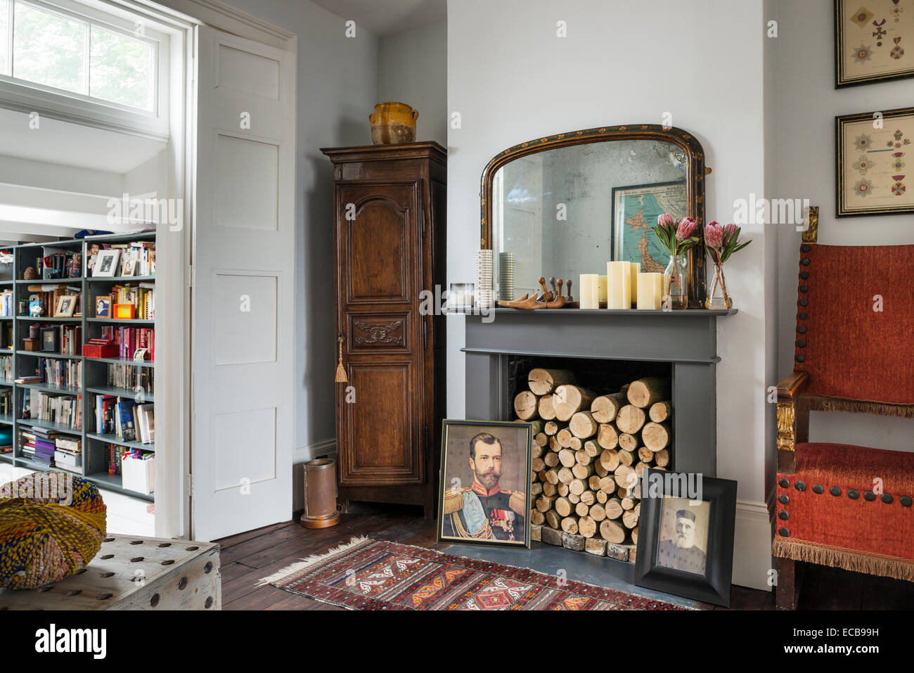 Tapis Vintage sur plancher en bois en face d'une cheminée avec des bûches et des portraits de famille Banque D'Images