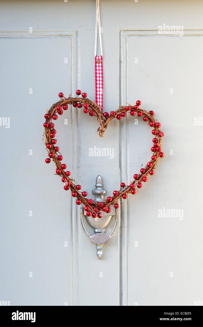 Coeur de fruits rouges couronne de Noël accroché sur une porte en bois Banque D'Images