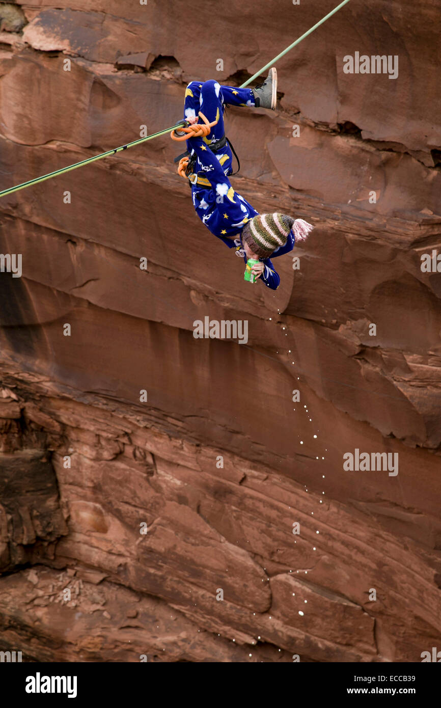 Femme boit une bière à l'envers sur une highline dans Moab, UT. Banque D'Images