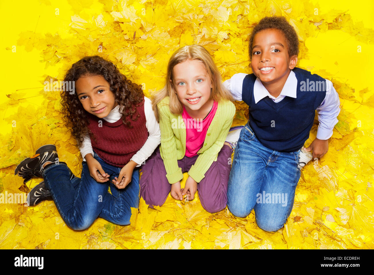 Groupe d'enfants assis sur les feuilles d'automne Banque D'Images