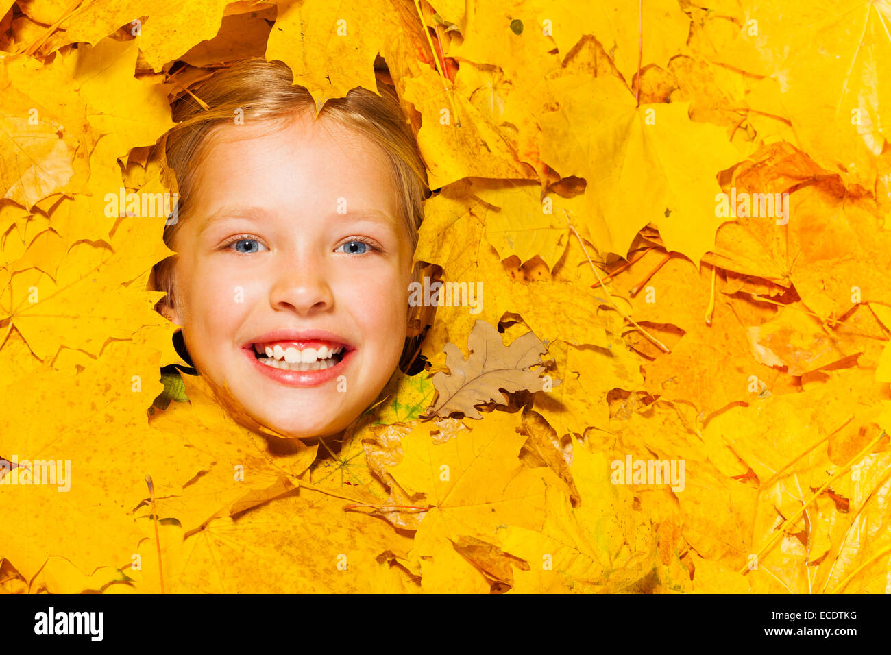 Visage de petite fille blonde souriante dans feuilles d'érable Banque D'Images
