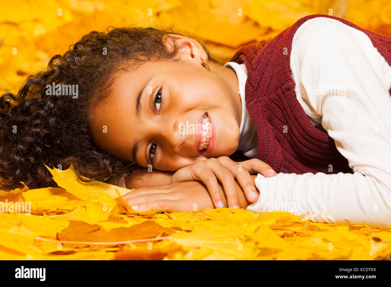 Petite fille africaine se pose sur les feuilles jaunes d'automne Banque D'Images