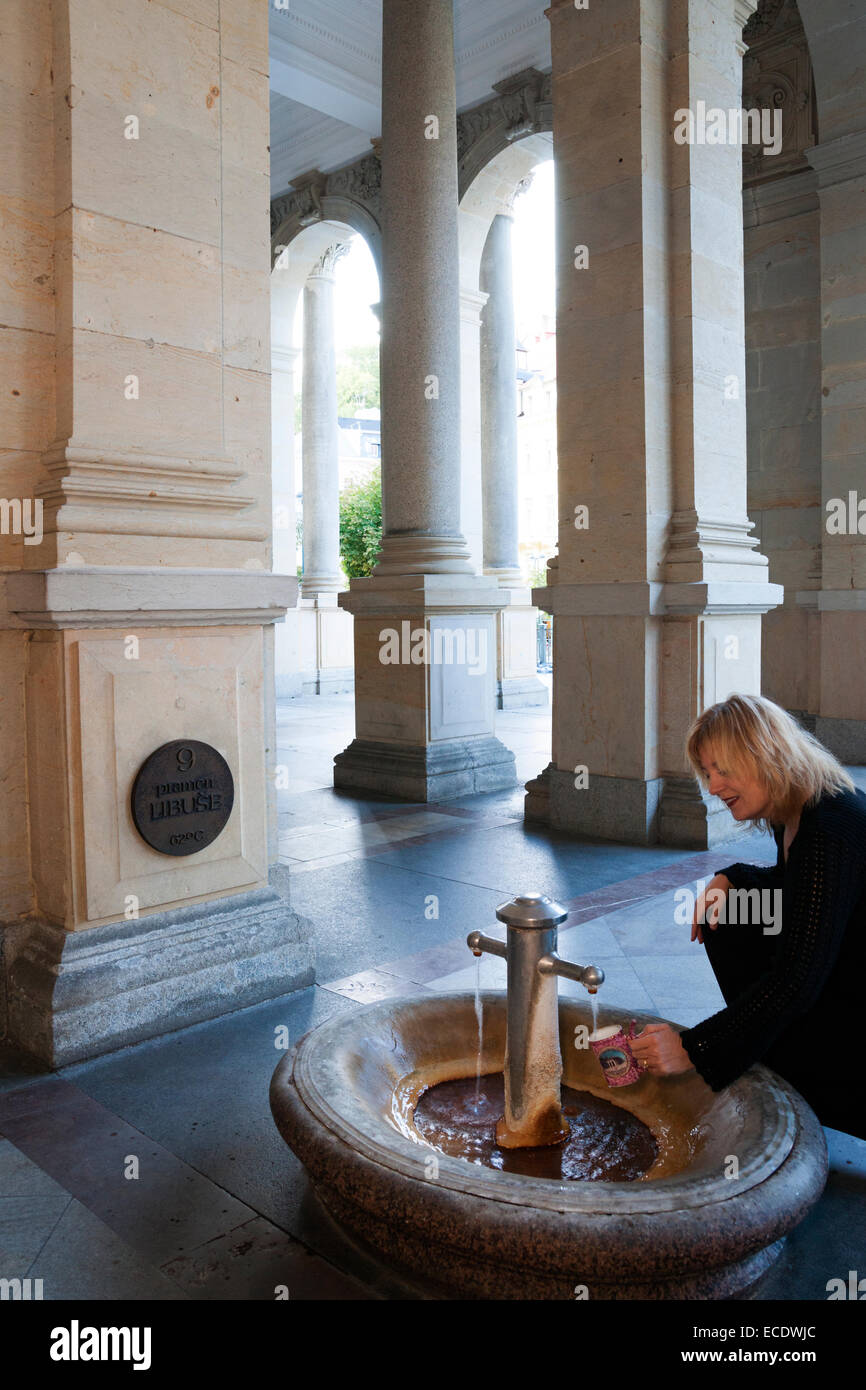 Femme blonde remplit une tasse en céramique typique avec des eaux thermales minérales sur l'un des cinq sources thermales de Moulin Colonnade, Karlovy Vary Banque D'Images