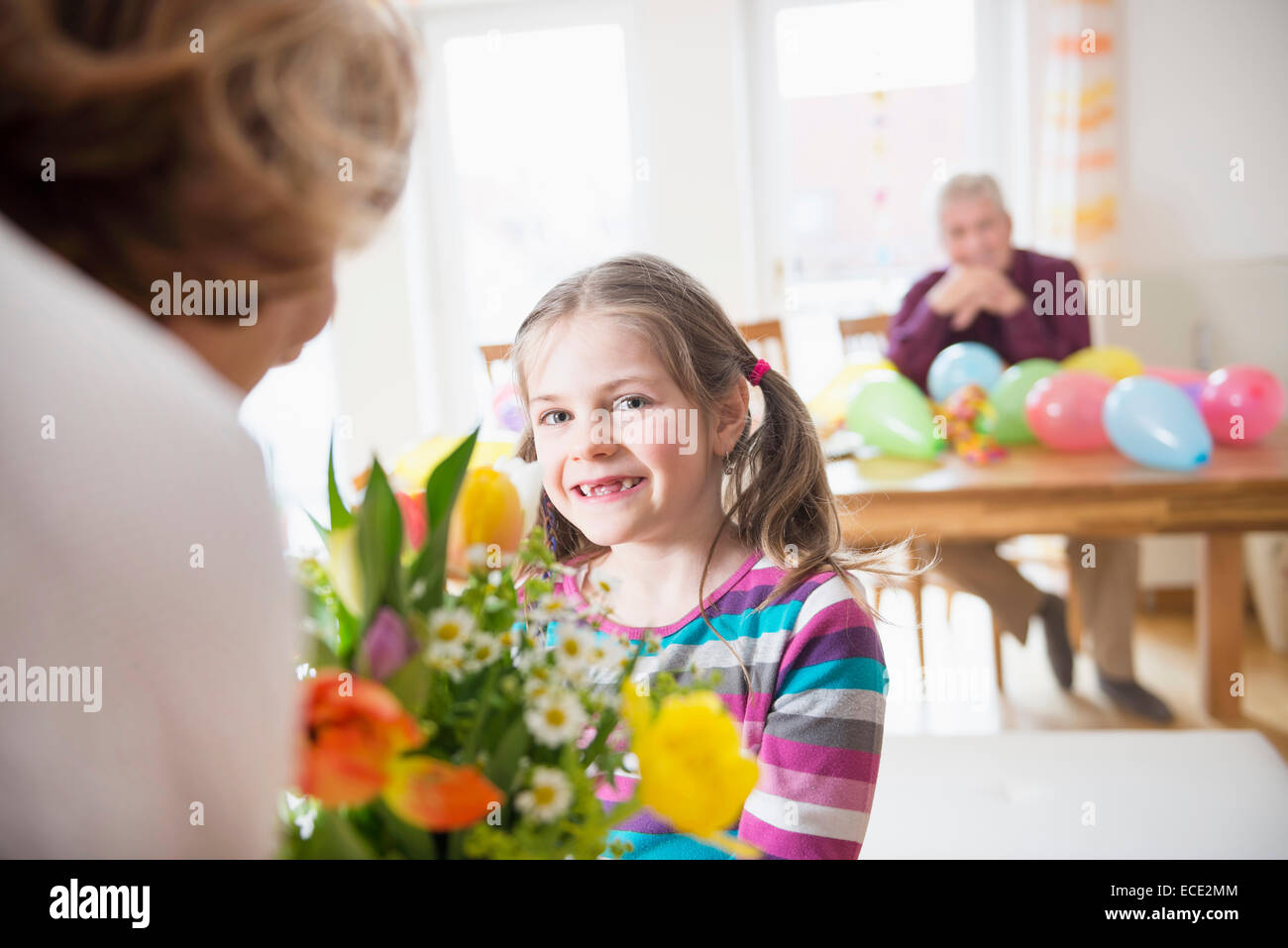 Petite-fille main sur bouquet de fleurs à sa grand-mère tandis que grand-père en arrière-plan Banque D'Images