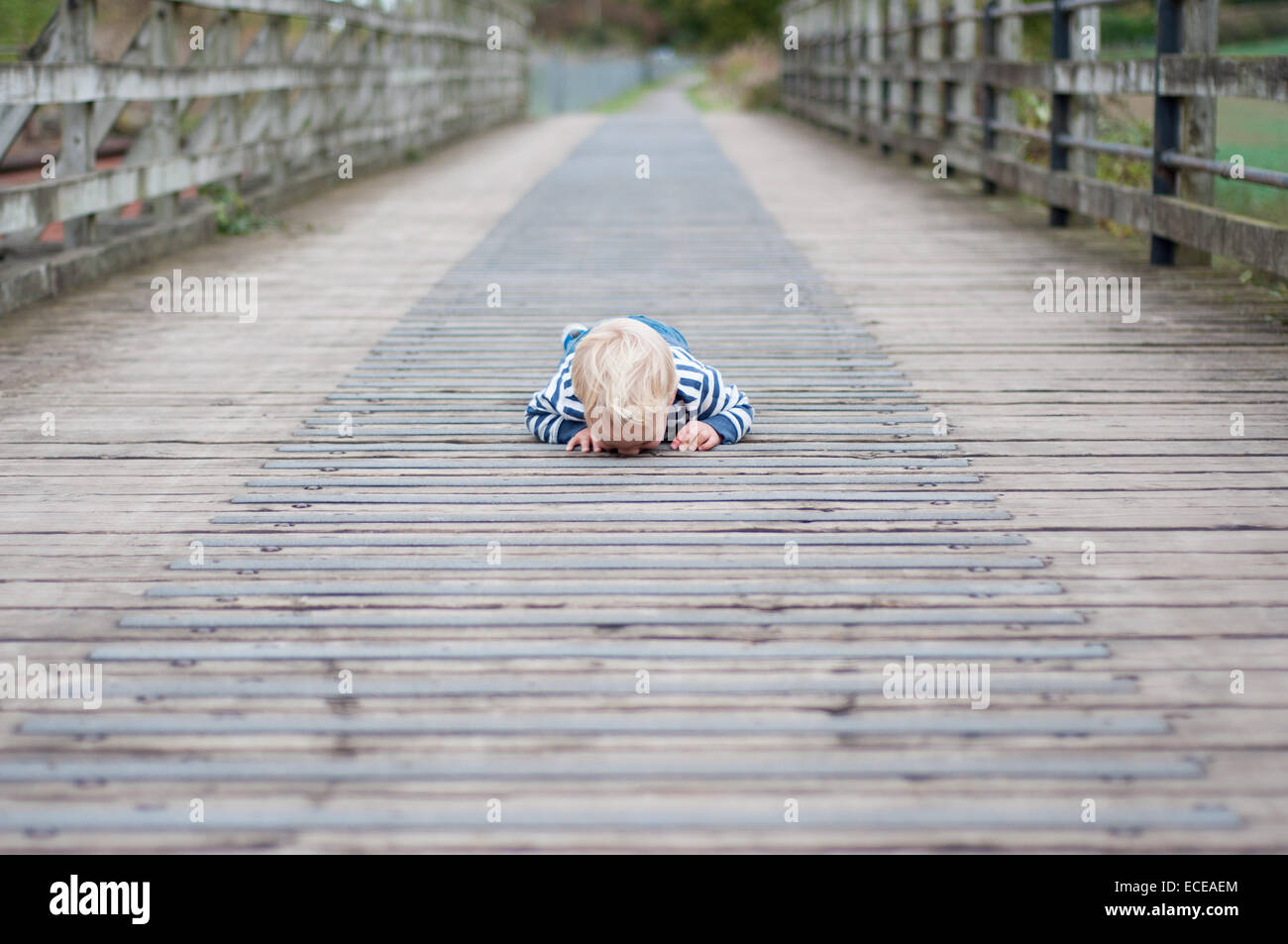 Garçon couché sur le pont à la recherche vers le bas à travers les fissures Banque D'Images