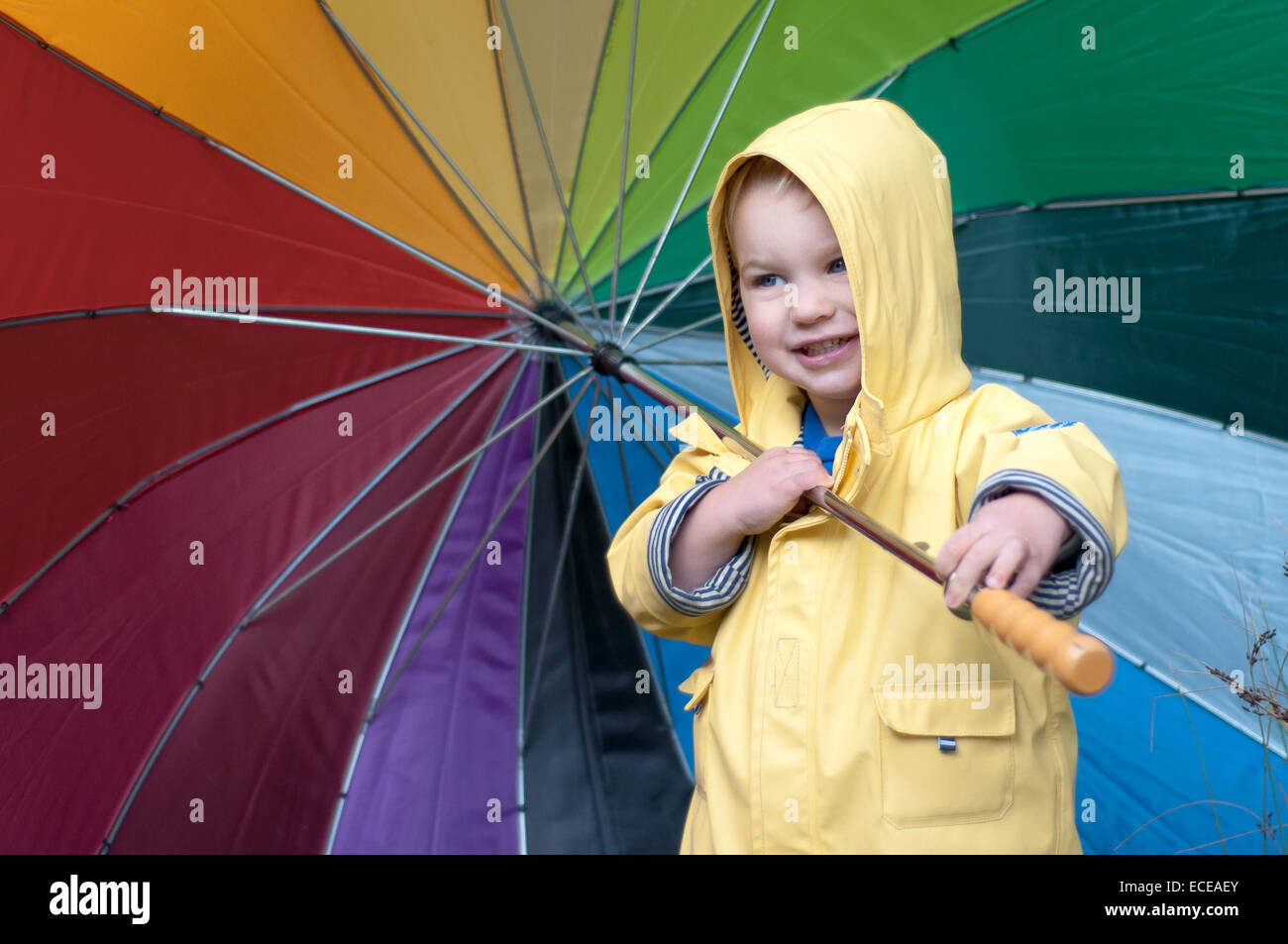 Garçon sous un imperméable portant un parapluie multicolore Banque D'Images