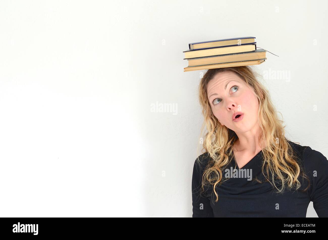 Femme à la recherche jusqu'à la pile de livres en équilibre sur la tête vintage Banque D'Images