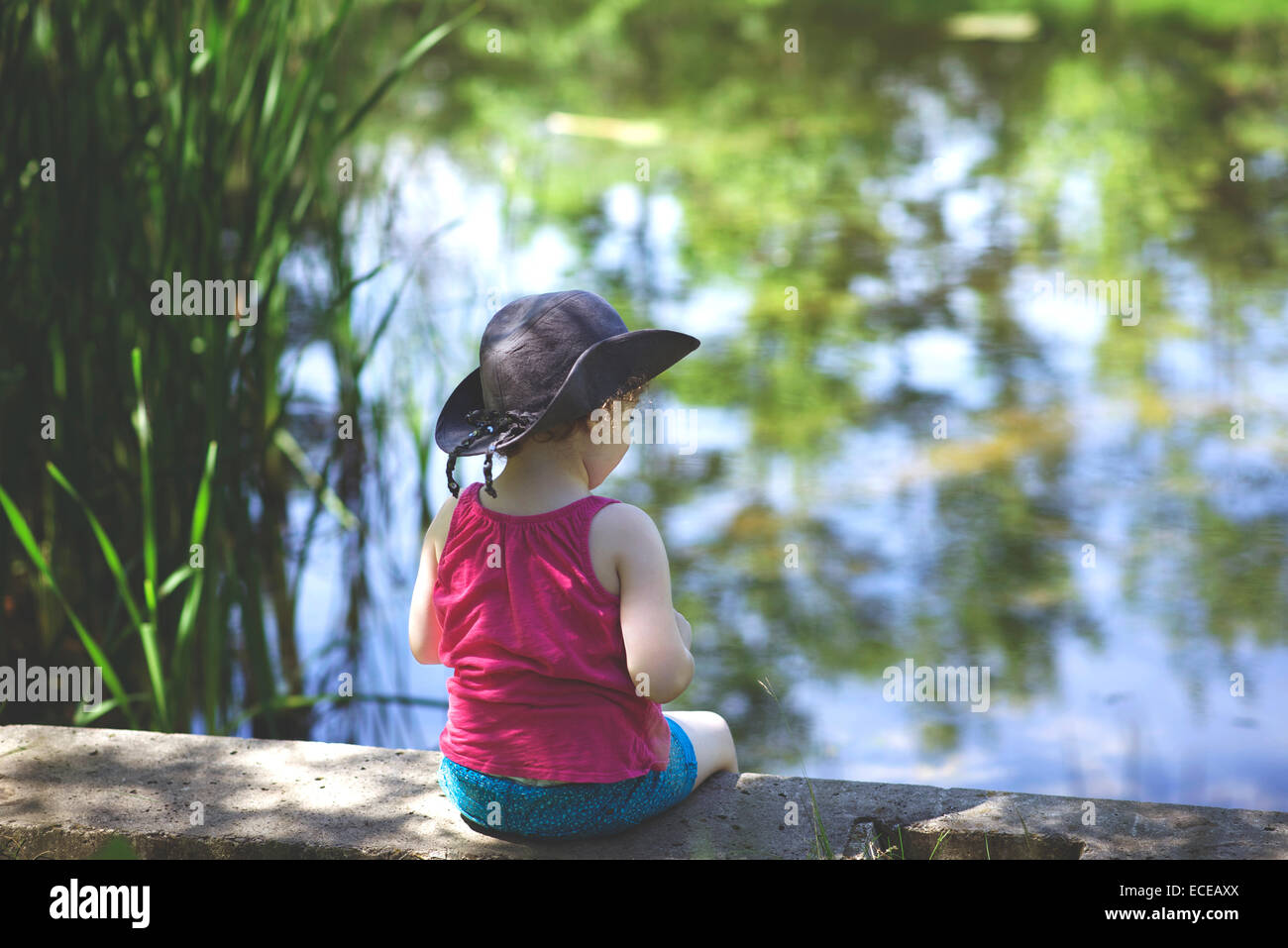 Girl (4-5) sitting par pond Banque D'Images