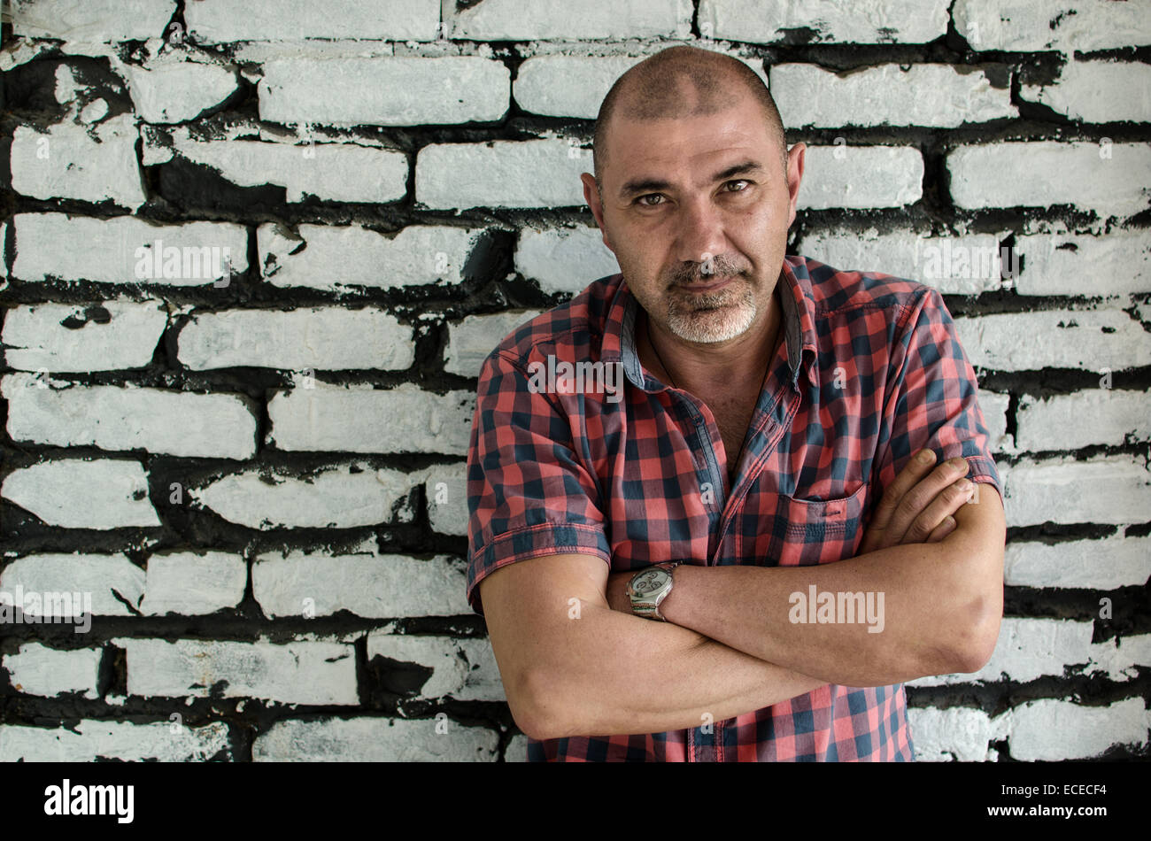 Portrait of a man with arms crossed standing par un mur de briques Banque D'Images