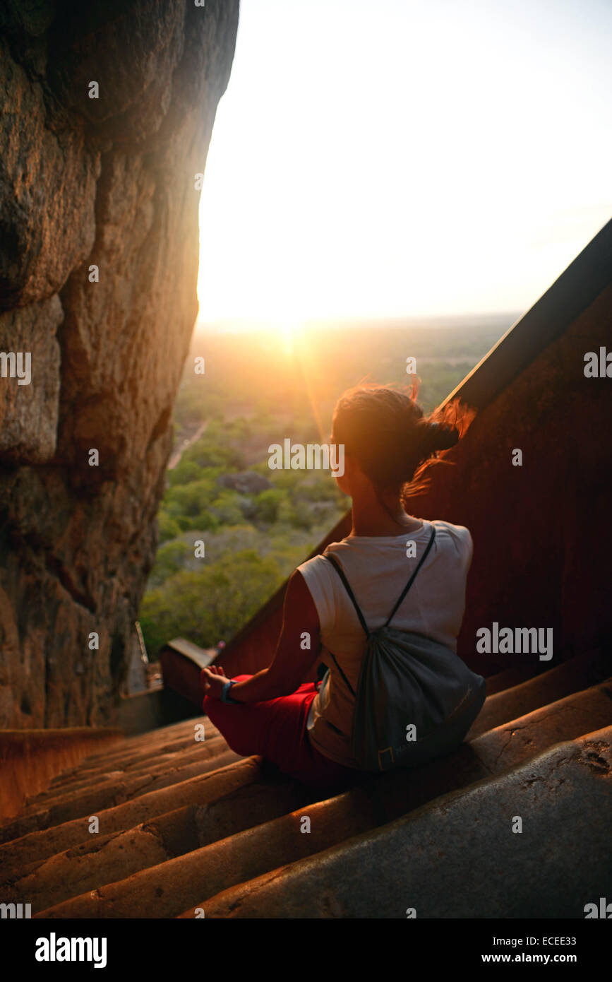 Jeune femme assise en lotus posent dans les escaliers jusqu'à la ville ancienne de Sigiriya, Sri Lanka Banque D'Images