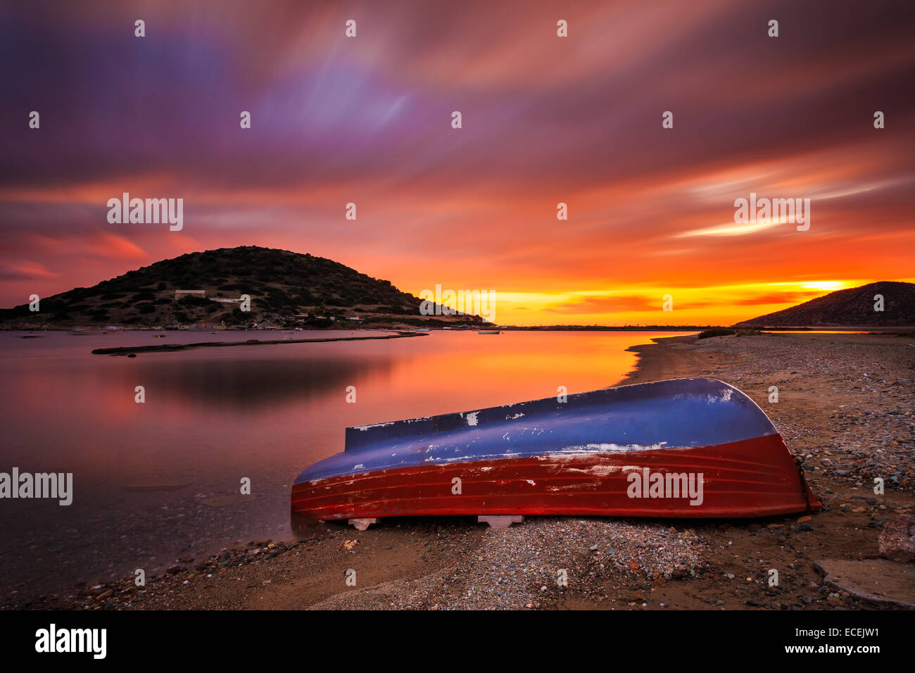 Bateau de pêche solitaire à gauche contre une côte spectaculaire et de soleil colorés avec des nuages de couleur passant sur le bateau Banque D'Images