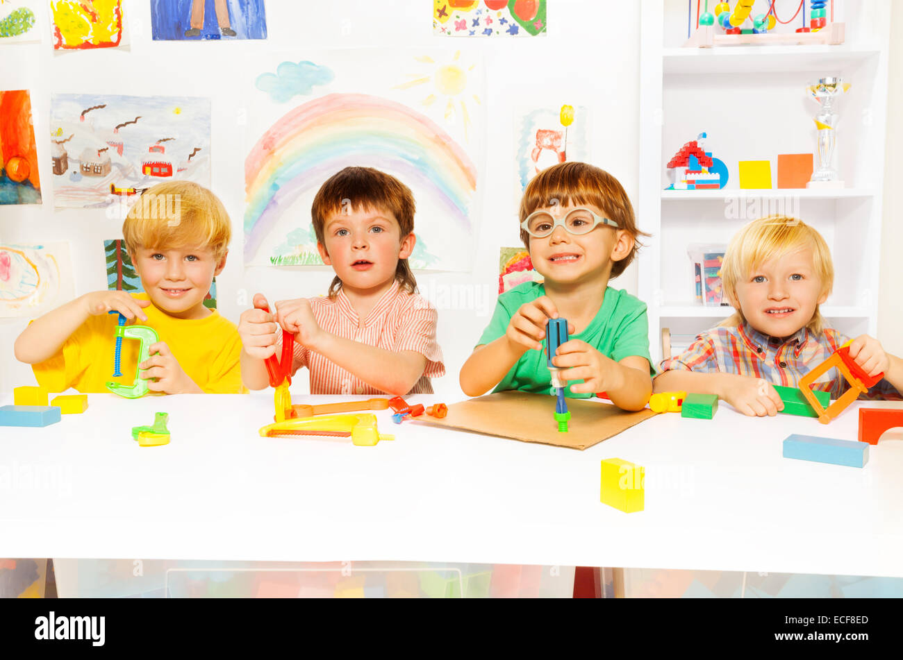 Groupe d'enfants d'âge préscolaire de la maternelle en jouant avec des outils en plastique en classe, avec un joli garçon dans les verres vissant bo Banque D'Images