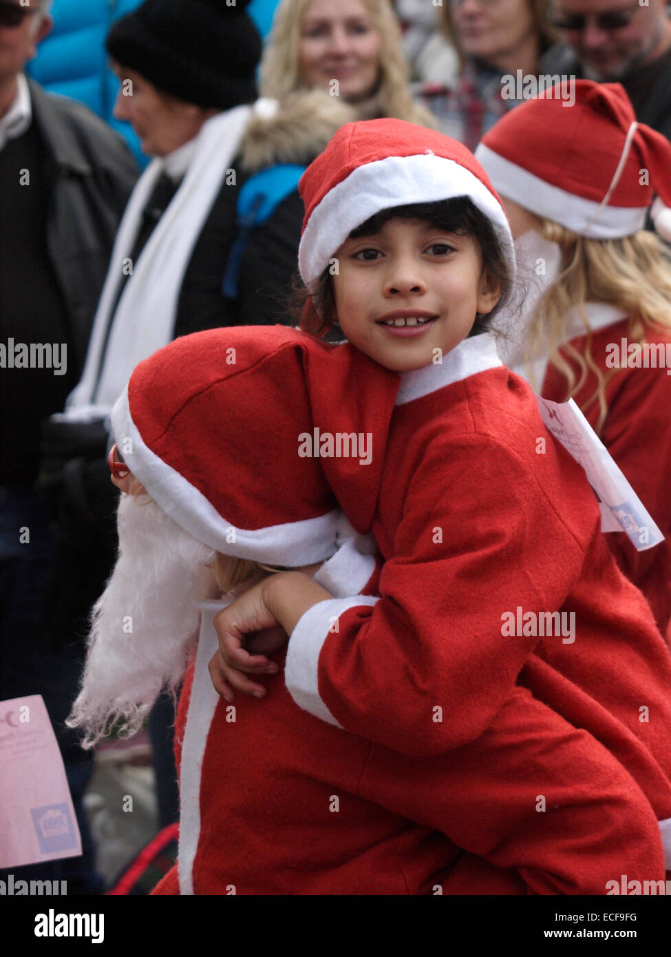 Donner un enfant à un autre enfant à dos, habillé en Père Nöel pour l'organisme de bienfaisance Santa run à l'festival de Noël de Padstow, Co Banque D'Images