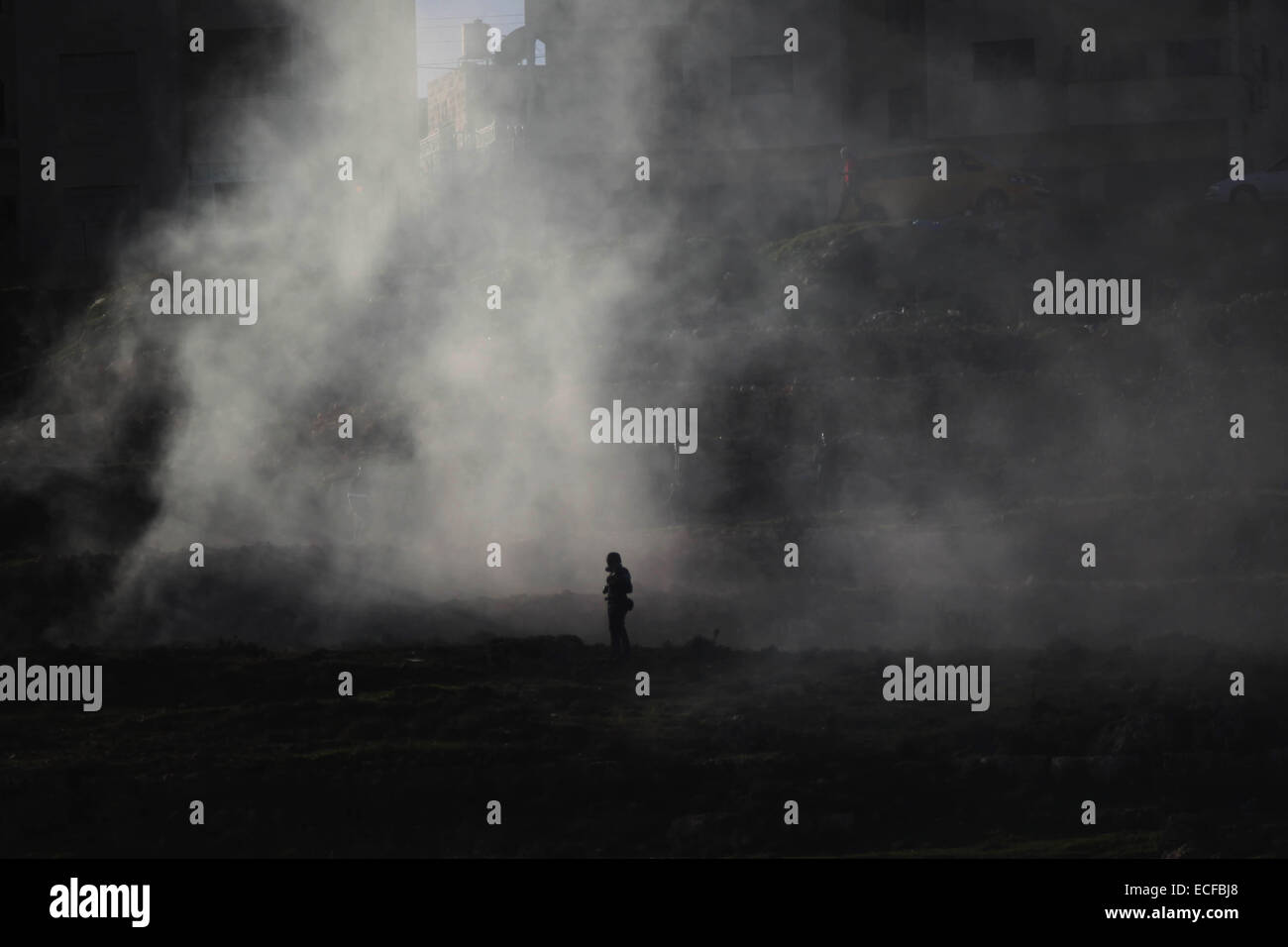 Ramallah, Cisjordanie, territoire palestinien. 13 Décembre, 2014. Un manifestant palestinien est de couvrir à partir de gaz lacrymogènes tirés par les forces de sécurité israéliennes au cours d'affrontements tout en protestant contre la mort de Ziad Abu Ein, un haut responsable palestinien qui sont morts dans un affrontement avec les troupes israéliennes, plus tôt cette semaine, près de la prison d'Ofer, près de la ville de Ramallah, en Cisjordanie, le 13 décembre 2014. Credit : ZUMA Press, Inc./Alamy Live News Banque D'Images