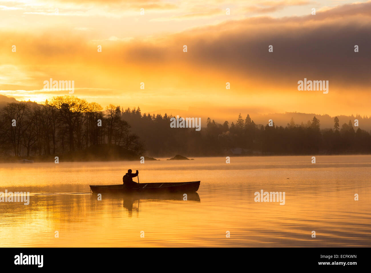 Le lever du soleil sur le lac Windermere à Ambleside, Lake District, UK, avec un homme une pagaie canoë canadien. Banque D'Images