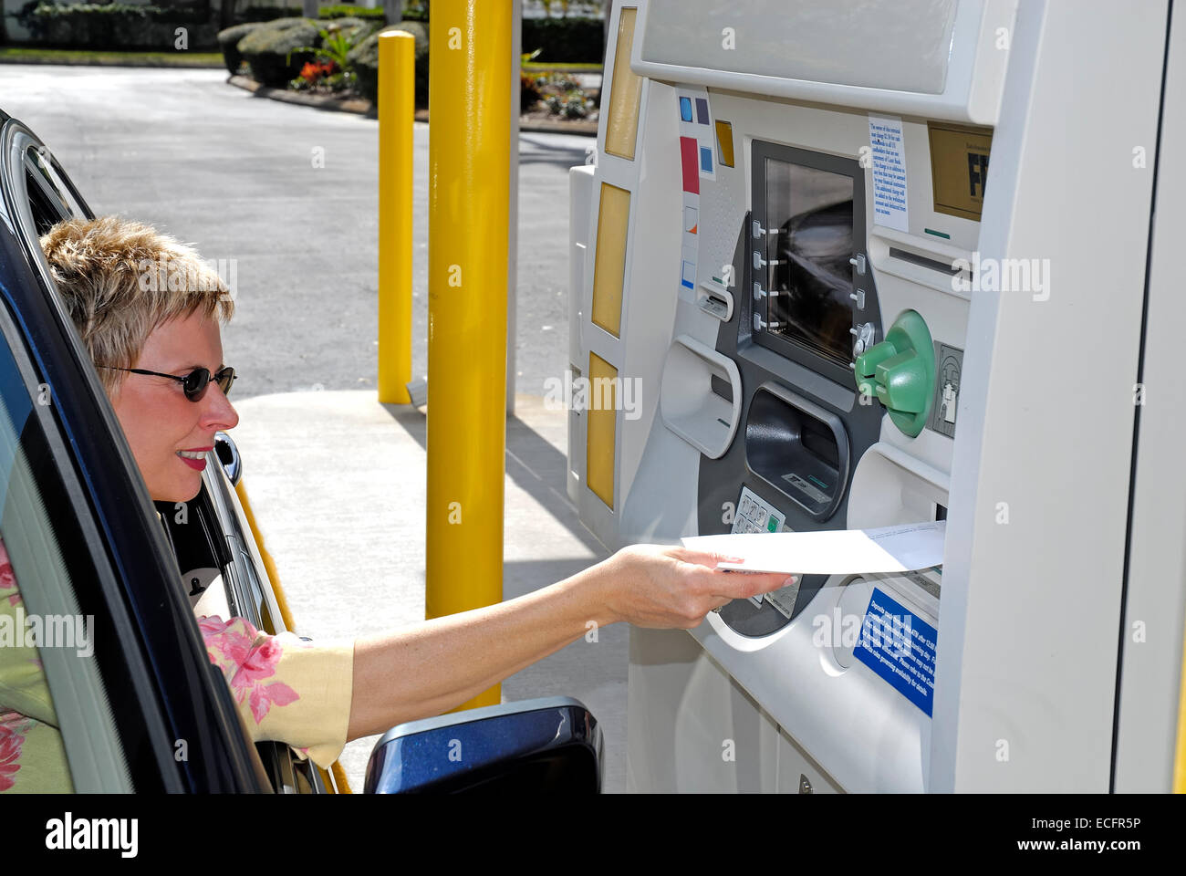 Young Caucasian woman dans une voiture à l'aide d'un lecteur de guichet automatique. Banque D'Images