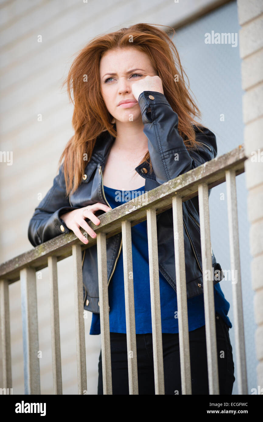 Un solo de moody triste jeune femme rousse aux cheveux gingembre adolescent  girl alone par elle-même s'appuyant sur un balcon à l'extérieur d'un bloc  d'appartements abandonnés abandonnés UK Photo Stock - Alamy