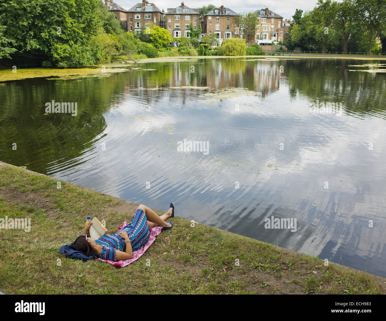 Lecture d'une femme par un lac sur Hampstead Heath à Londres UK Banque D'Images