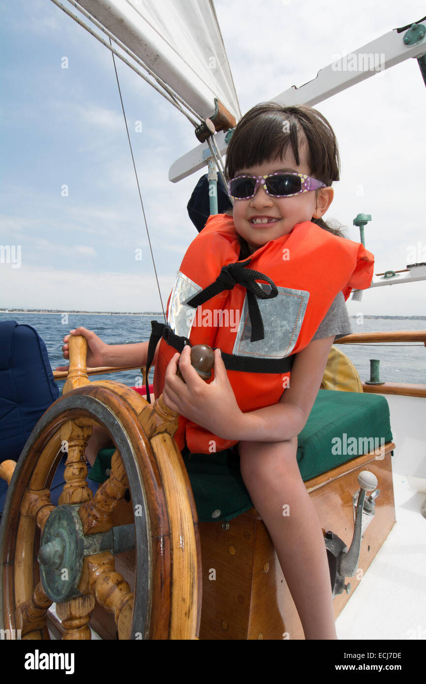 Un 7-year-old girl à la barre d'un voilier en bois. Banque D'Images