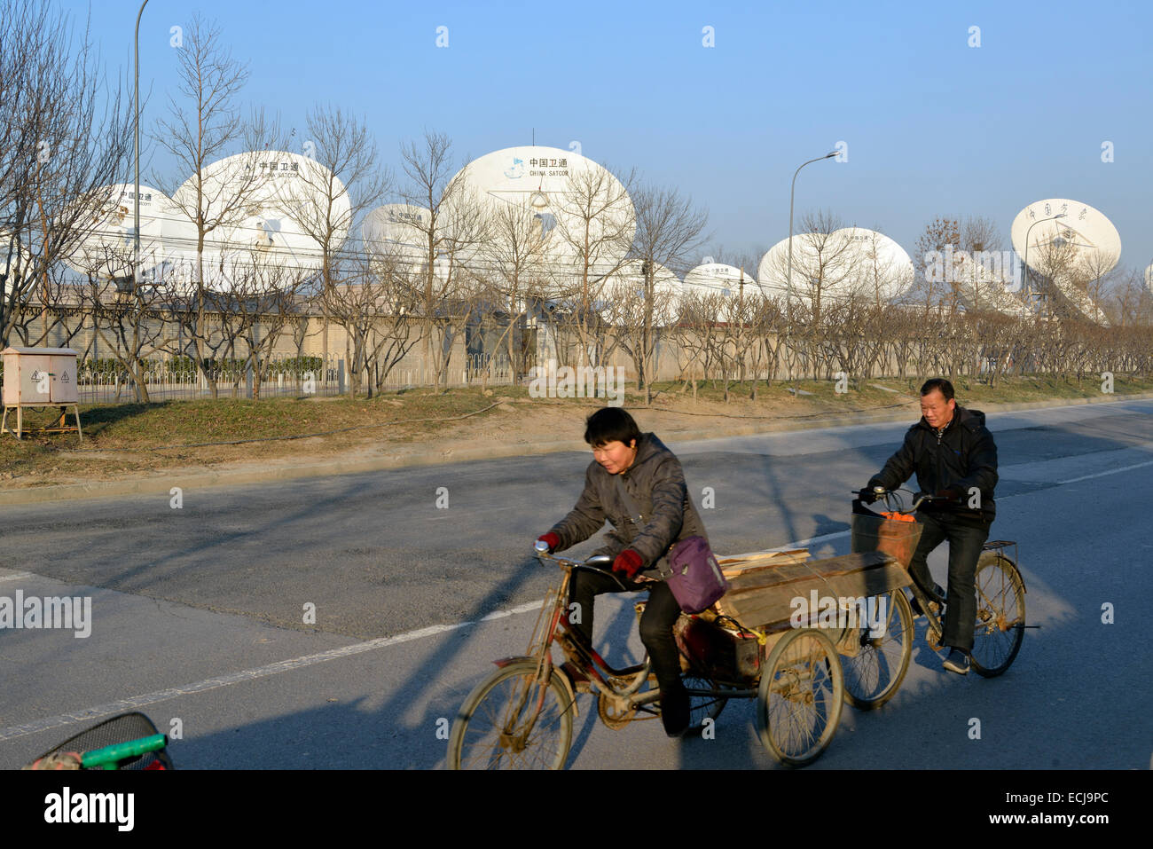Les cyclistes passé récepteurs satellite à China Satellite Communications Co.,Ltd(China Satcom) à Pékin, Chine Banque D'Images