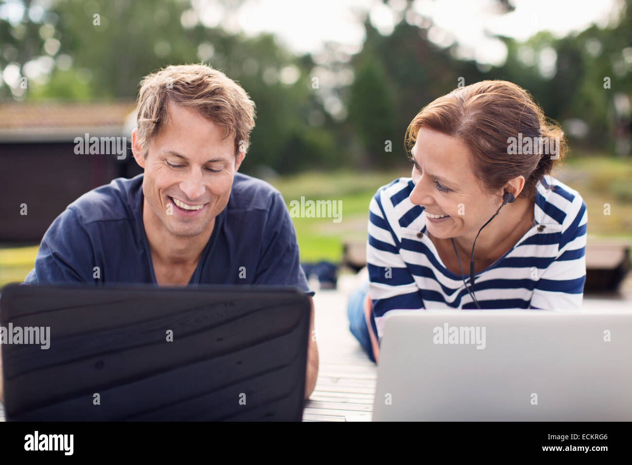 Smiling mature couple moyen d'ordinateurs portables tout en se trouvant sur pier Banque D'Images