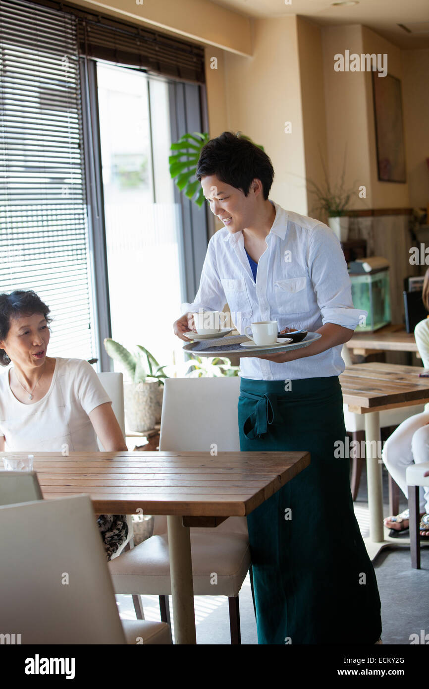 Waiter serving une femme assise à une table dans un café. Banque D'Images