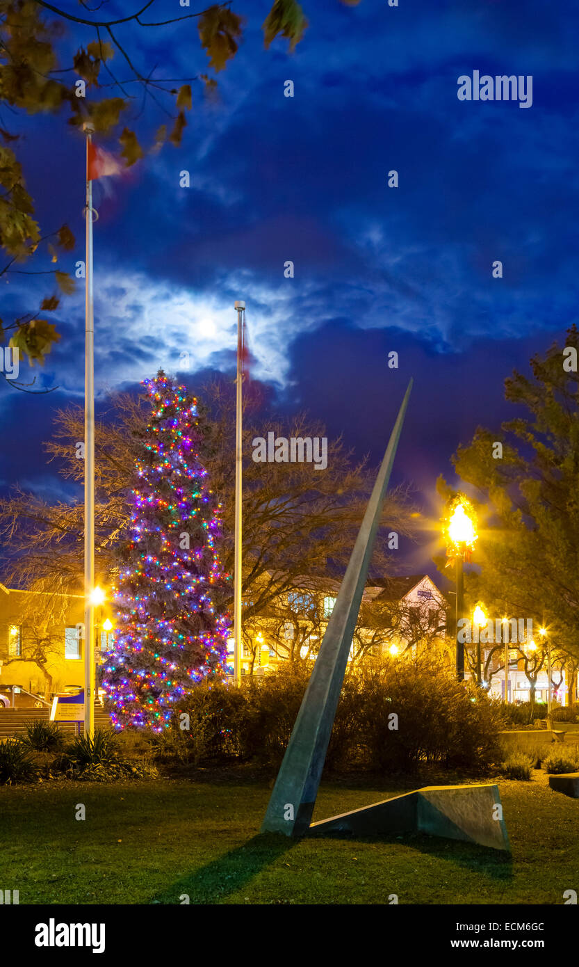 Un très grand arbre de Noël (sapin bleu) couvert de lumières avec une sculpture d'art au premier plan. Oakville, Ontario, Canada. Banque D'Images