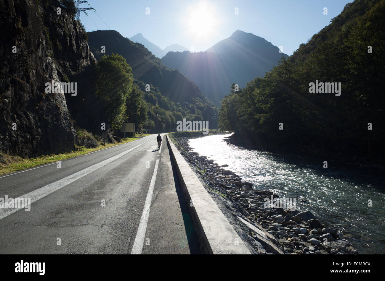 Cycliste solitaire dans le soleil d'équitation sur une route vide à côté d'une rivière avec montagnes Pyreneean imminente dans l'arrière-plan Banque D'Images